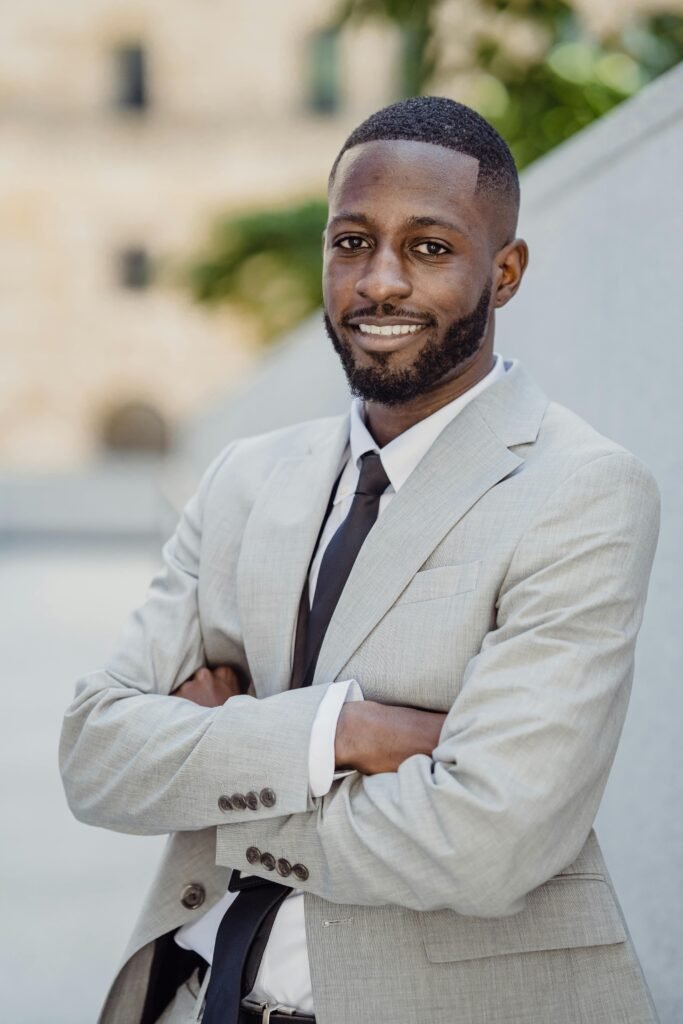 pexels-photo-13801614-13801614 A confident businessman in a gray suit, smiling and posing outdoors with arms crossed.